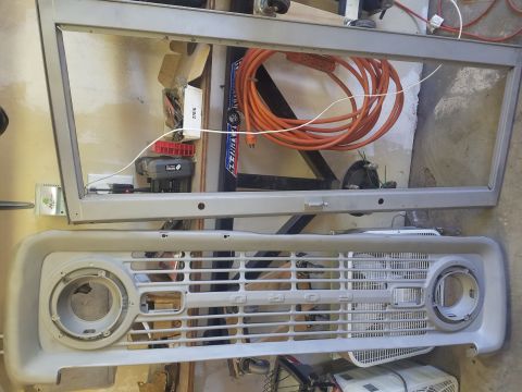 1968 Ford Bronco - A disassembled 1968 Ford Bronco front end is laid out on a garage floor. The grille and headlight surrounds are visible, along with the fra…