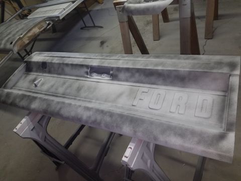 1968 Ford Bronco - A Ford tailgate is shown being prepped for paint, resting on sawhorses. The tailgate has the embossed "FORD" lettering visible.
