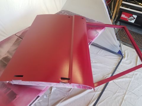 1968 Ford Bronco - A red car door and its frame are shown in a workshop setting, possibly during a painting or restoration process. The door appears to be a c…