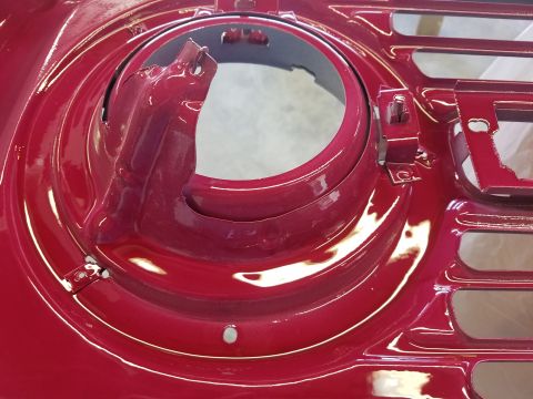 1968 Ford Bronco - A close-up view of a shiny, red painted vehicle part, likely a headlight bucket or grille surround, showing a circular opening and mounting…