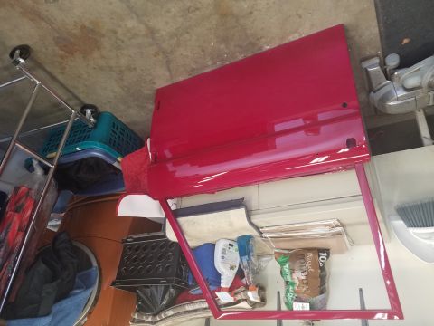 1968 Ford Bronco - A bright red car door is leaning against a shelving unit. The door is partially disassembled, with a metal frame visible underneath.