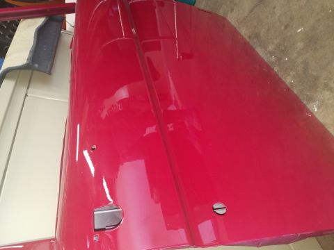 1968 Ford Bronco - A shiny, red, uninstalled vehicle door is laid out on a concrete floor next to a cream-colored vehicle body panel. The door has visible mou…