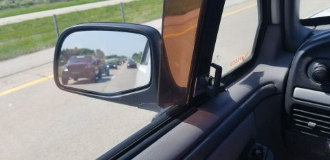 1995 Ford Bronco - View from the driver's side window of a dark-colored SUV towing a trailer in traffic, as seen in the side mirror. The vehicle is on a highw…
