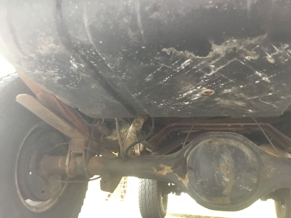 Underside of a vehicle showing rear axle, leaf springs, and fuel tank with rust.