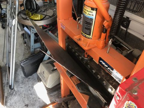 1992 Jeep Wrangler - A close-up view of an orange hydraulic bottle jack mounted on a metal frame. A long, thin piece of metal is positioned beneath the jack, su…