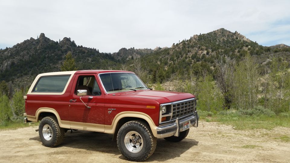 Red and tan Ford Bronco parked on dirt road with mountains in background.