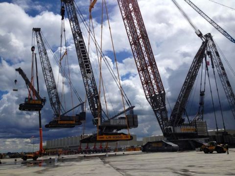 1992 Ford Bronco - Multiple large construction cranes are assembled and positioned on a paved surface under a cloudy sky. One crane is actively lifting a sect…