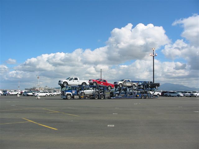 Car carrier truck loaded with new pickup trucks and SUVs in an open lot.