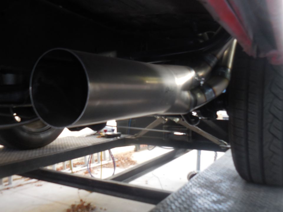 Custom exhaust system with polished pipes and welds under a vehicle.