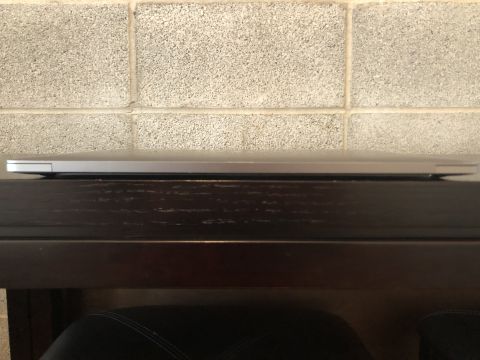 1989 Ford Bronco - The side profile of a closed silver laptop is resting on a dark wooden surface against a light gray cinder block wall.