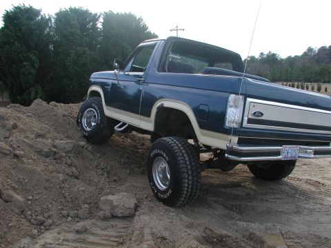 1985 Ford Bronco - This lifted Ford Bronco navigates a sandy incline, showing its off-road capabilities.