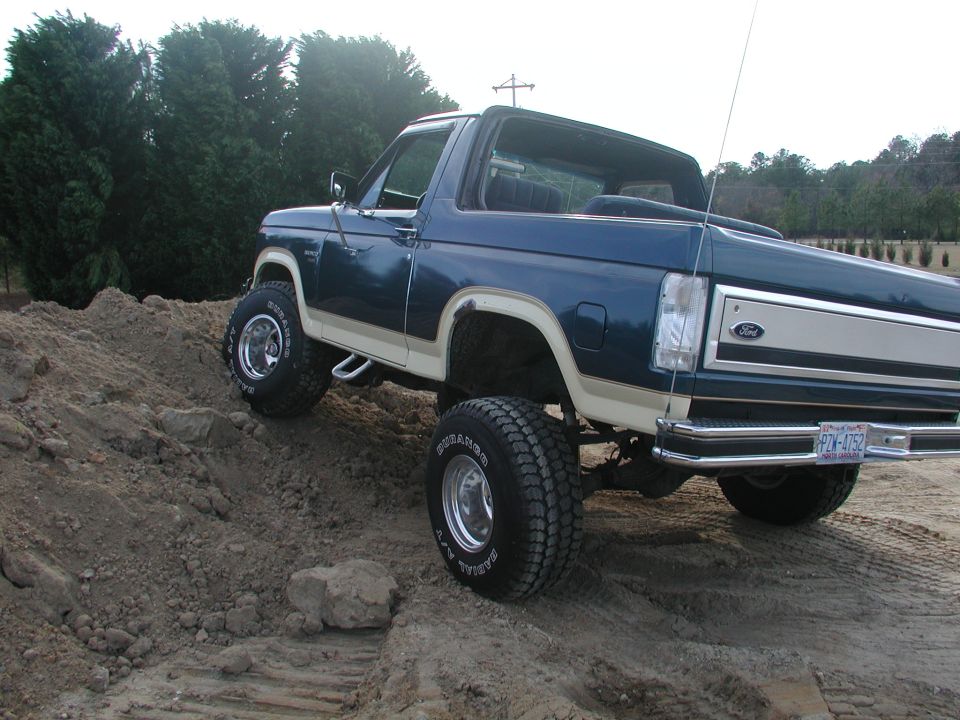 Blue Ford Bronco with tan trim, lifted on off-road tires, climbing a dirt mound