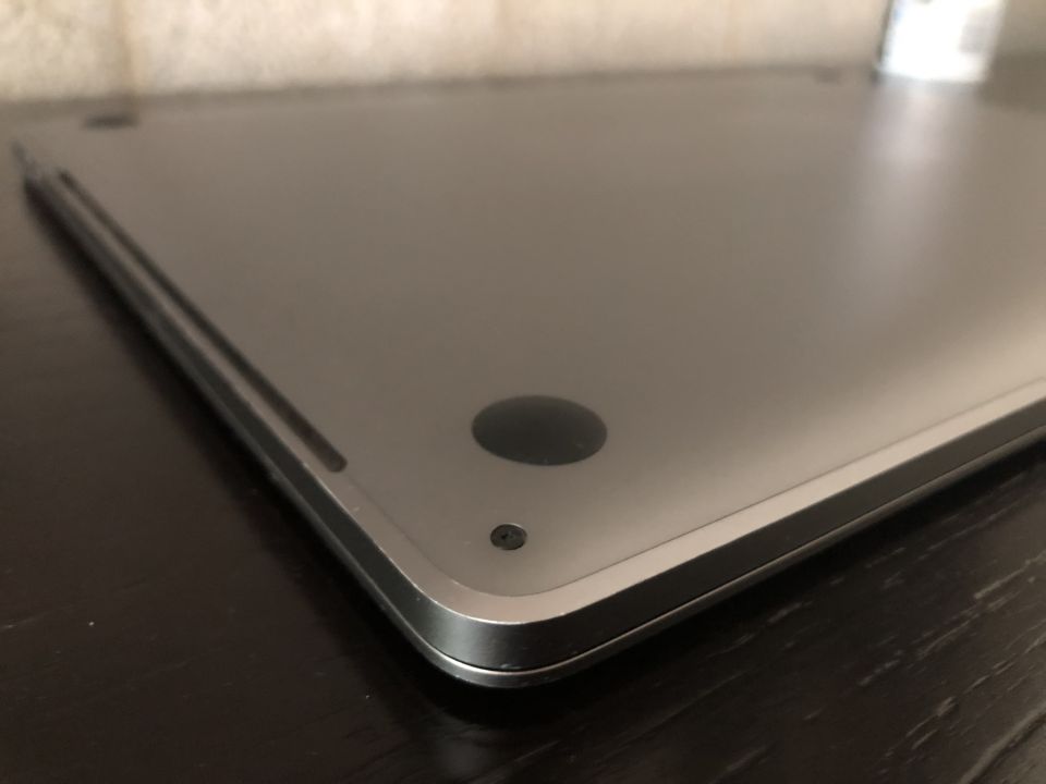 Underside of a silver laptop with a black rubber foot on a dark wooden table.