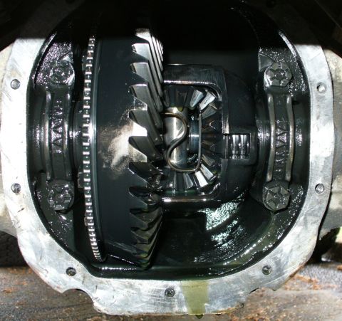 1992 Ford Bronco - A close-up view of the differential gears inside a vehicle's rear axle housing, lubricated with dark oil. The image shows the ring gear, pi…