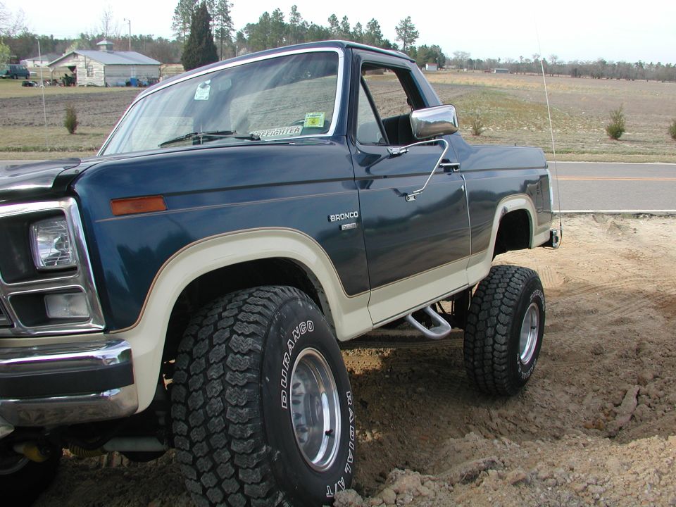 Dark blue and tan Ford Bronco with lifted suspension and off-road tires, viewed from the front three-quarter angle