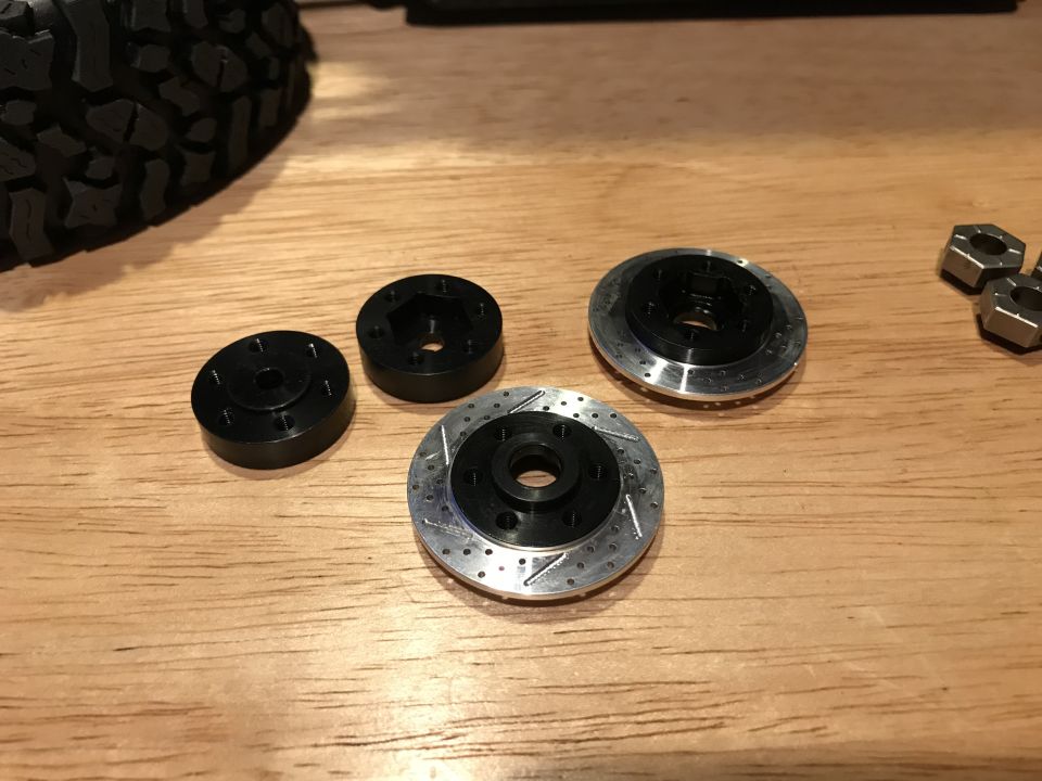 Scale model brake rotors and calipers on a wooden surface with a tire in the corner.