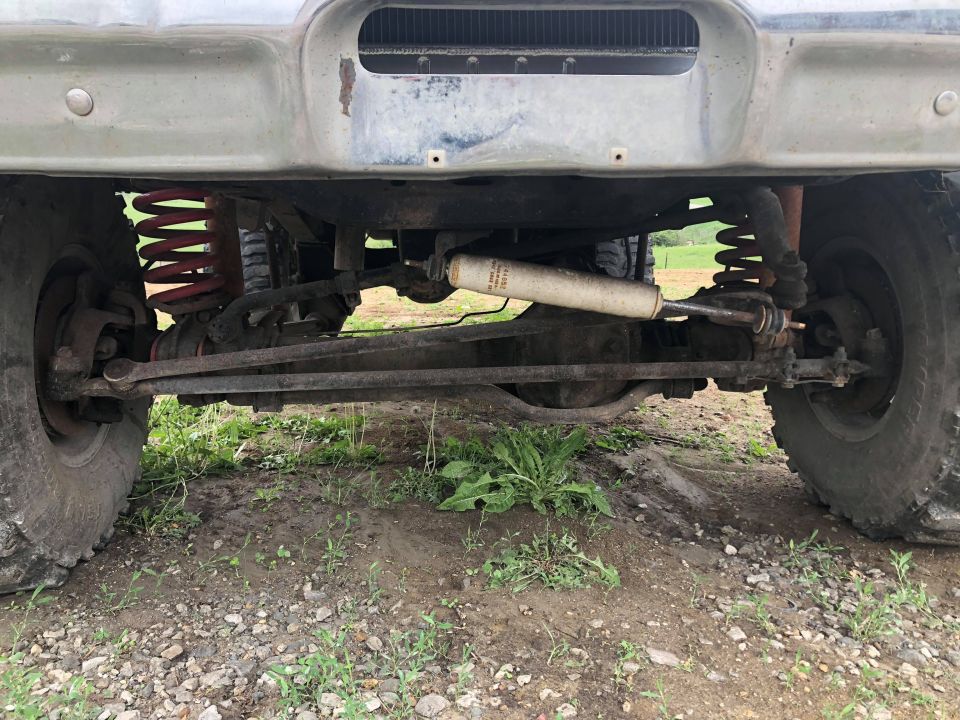 Underside of a vintage Ford Bronco front suspension with red springs and off-road tires.