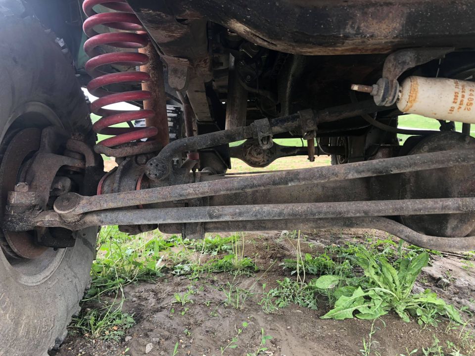 Underside of a vehicle showing red coil spring, shock absorber, and suspension linkages.