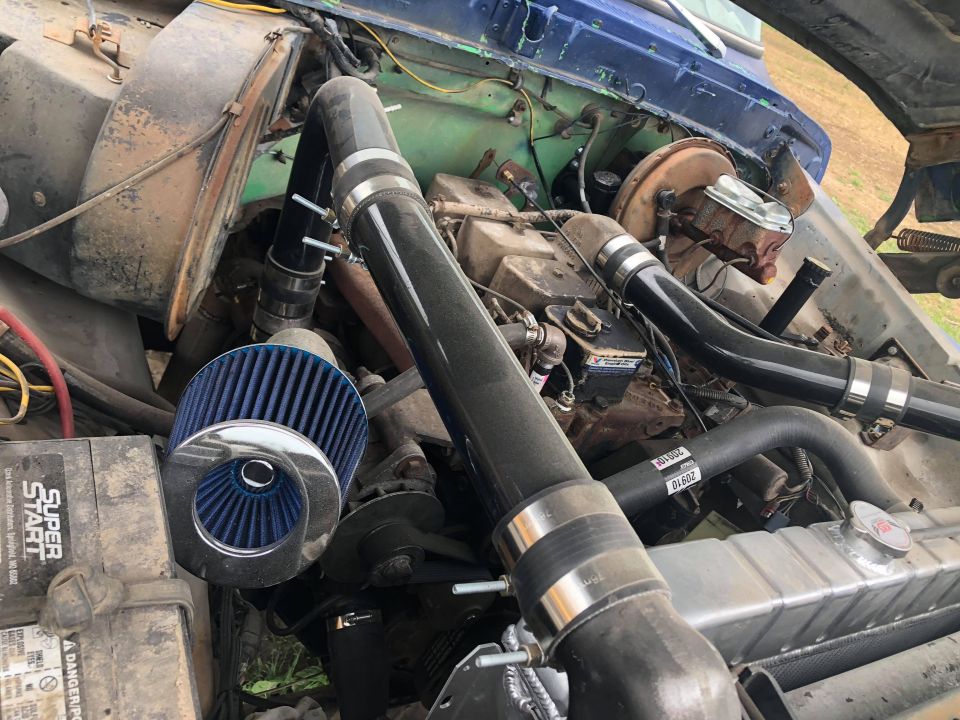 Engine bay of a classic Ford Bronco with blue air filter and black intake pipes.