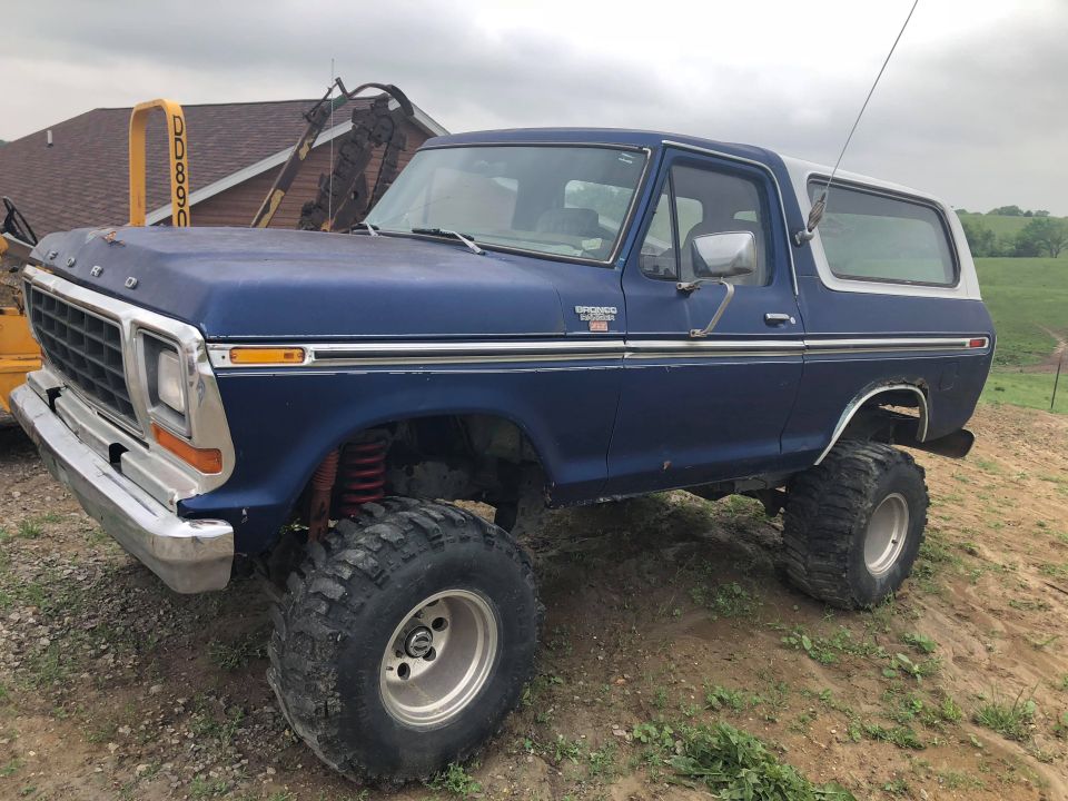 Lifted dark blue 1979 Ford Bronco with white top and large off-road tires on a dirt mound.