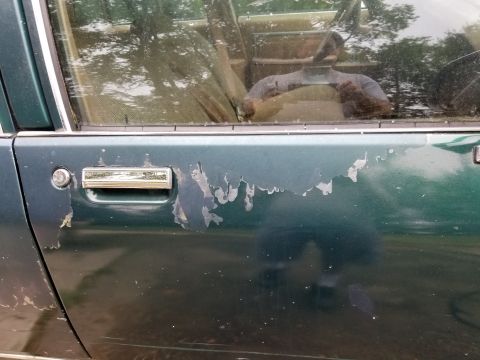 2001 Ford Crown Victoria - Peeling paint on the side door of a dark green vehicle, with a reflection in the window.