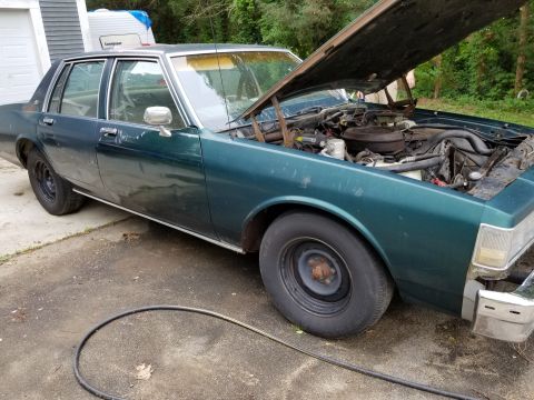 2001 Ford Crown Victoria - This green sedan has its hood open, revealing the engine compartment. The vehicle appears to be in a driveway with a garage in the backgrou…