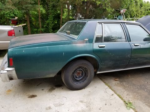 2001 Ford Crown Victoria - This green sedan, likely from the 1980s, is parked next to a silver pickup truck.