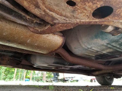 2001 Ford Crown Victoria - The heavily rusted undercarriage of a vehicle is visible, with exhaust pipes and a fuel tank prominent.