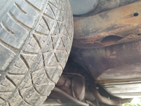 2001 Ford Crown Victoria - Undercarriage view showing a tire and exhaust system, with visible rust on the frame.