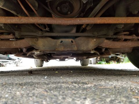 2001 Ford Crown Victoria - The undercarriage of a vehicle shows rusted suspension parts and frame components.