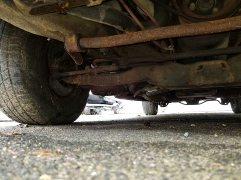 2001 Ford Crown Victoria - A low-angle shot reveals the rusty undercarriage components, including the suspension and exhaust, of a vehicle.