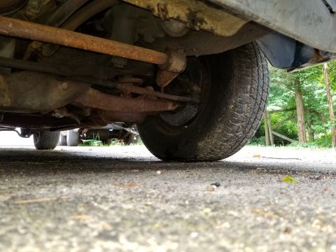 2001 Ford Crown Victoria - Low angle shot of a car's undercarriage and tire, with another vehicle in the distance.