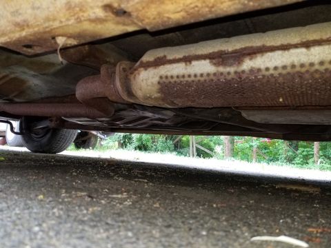 2001 Ford Crown Victoria - The exhaust system and undercarriage of a vehicle are shown, with visible rust and a tire in the frame.