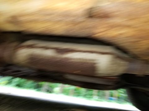 2001 Ford Crown Victoria - Close-up view of a rusted exhaust pipe and heat shield on the underside of a vehicle.