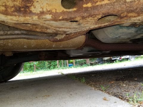 2001 Ford Crown Victoria - The underside of a car shows significant rust and corrosion on the chassis and exhaust components.