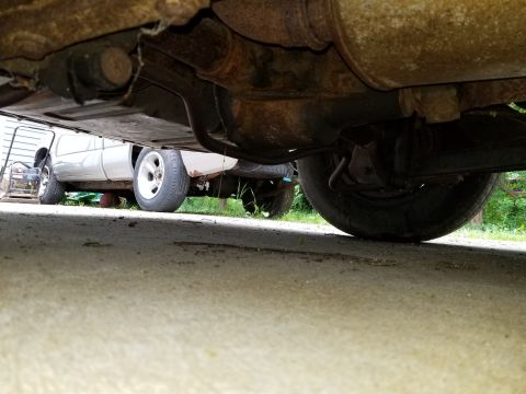 2001 Ford Crown Victoria - The underside of a vehicle shows significant rust and wear, with another vehicle partially visible behind it.