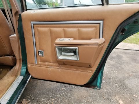 2001 Ford Crown Victoria - The interior door panel of a car shows wear and tear, with a tan upholstery and chrome accents.