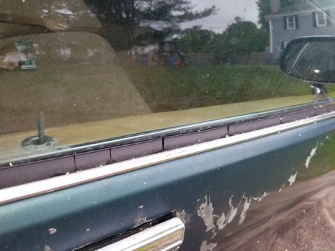 2001 Ford Crown Victoria - The side of a green car shows significant paint damage and a chrome door handle.