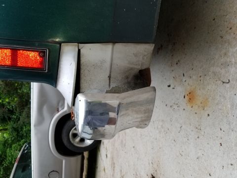 2001 Ford Crown Victoria - A damaged rear bumper and taillight are visible on a green vehicle, with another car behind it.