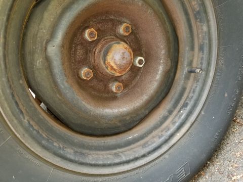 2001 Ford Crown Victoria - A close-up view of a rusty wheel hub with five lug nuts and a tire that appears to be flat or deflated.