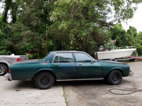 2001 Ford Crown Victoria - A dark green sedan with a boxy body style is parked outdoors next to a boat on a trailer.