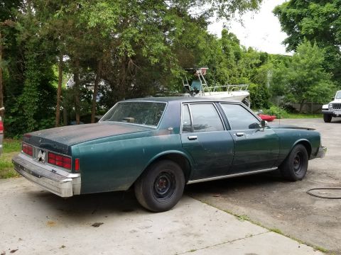 2001 Ford Crown Victoria - This 1989 Chevrolet Caprice sedan is parked outside next to trees and a boat.