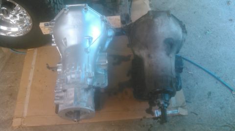 1992 Ford Bronco - Comparison of two transmissions, one appearing new and the other used, with a tire and wheel in the background.