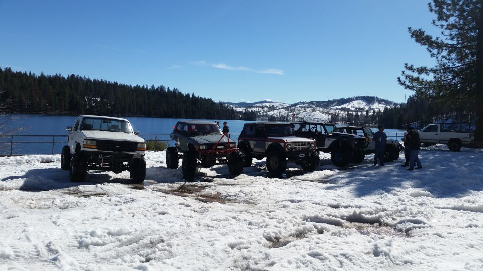 Several modified off-road vehicles parked in a snowy landscape next to a body of water