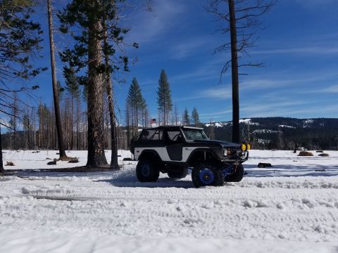 1968 Ford Bronco - A modified Ford Bronco navigates a snowy landscape, kicking up snow as it drives.