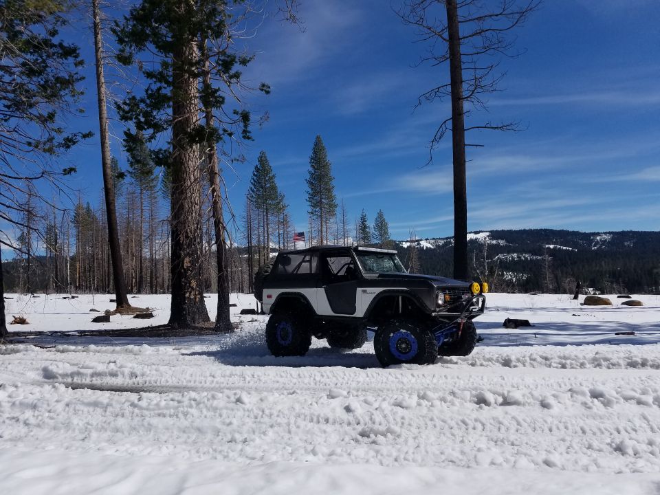 Modified Ford Bronco driving in snow with trees and mountains in background