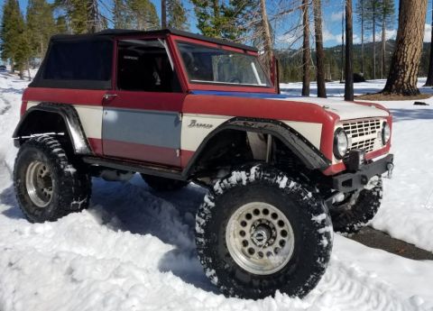 1968 Ford Bronco - A red and white 1968 Ford Bronco sits in a snowy landscape with trees in the background.