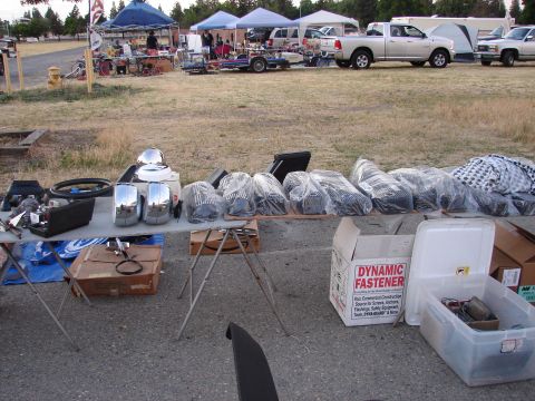 1973 Ford Ranchero - Various automotive parts, including chrome side mirrors, are displayed on tables at an outdoor market with vehicles in the background.