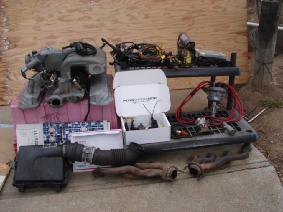 Engine intake manifold, air intake hose, exhaust manifolds, distributor, and wiring harness laid out on concrete