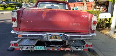 1966 Ford Ranchero - The rear of a red pickup truck is loaded onto a trailer, showing its taillights and license plate.
